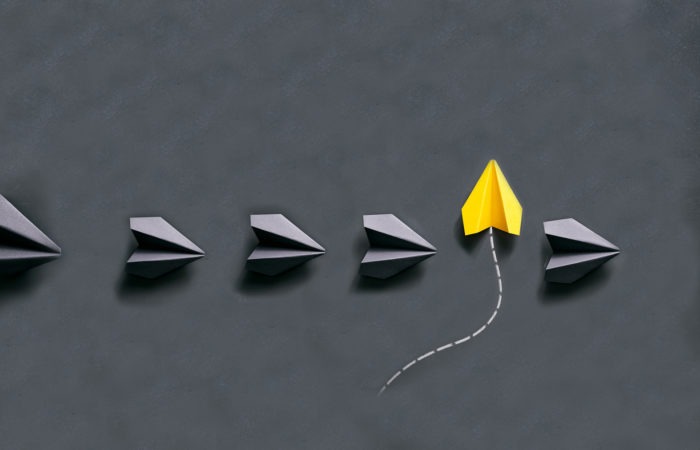 yellow paper plane in different direction to black paper planes